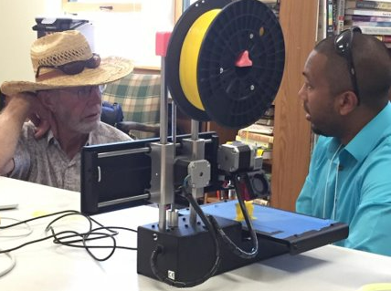 two men sit near a 3D printer
