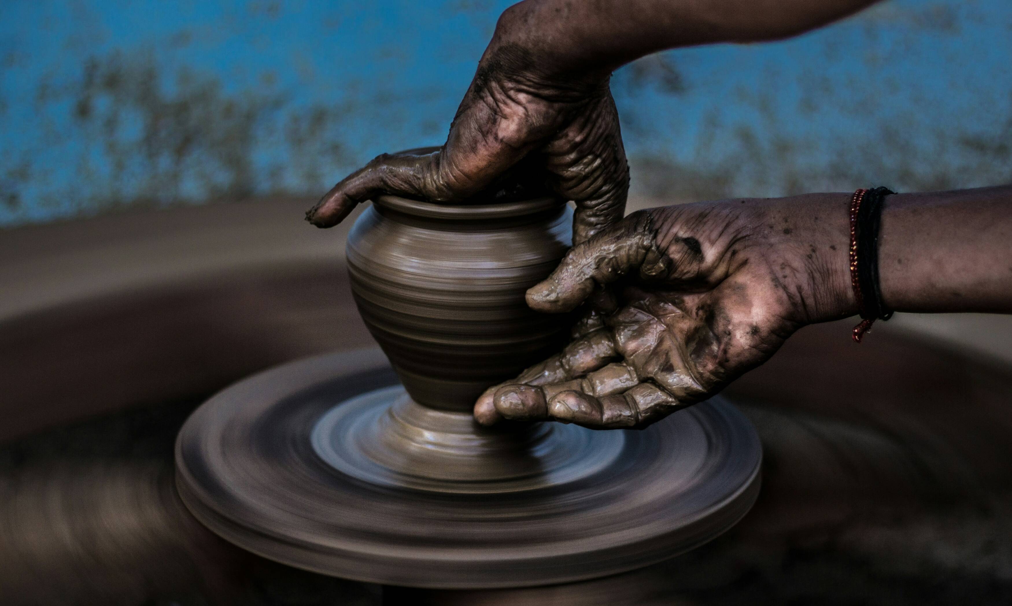 Two hands covered in clay form a pot on a spinning wheel.