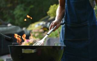 Color photograph of BBQ grill flame and person with spatula wearing apron
